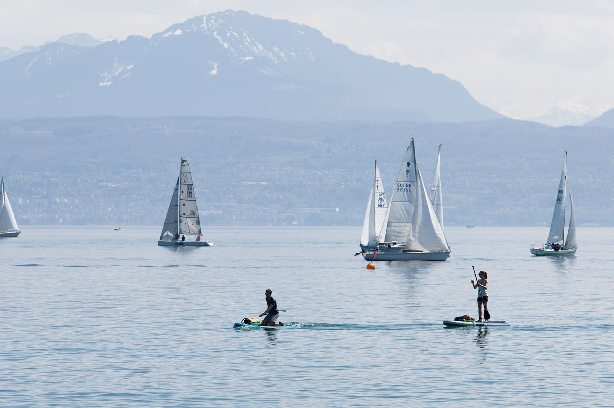 Sailboats and paddleboarders enjoying a sunny day on Lake Geneva with Alpine views.