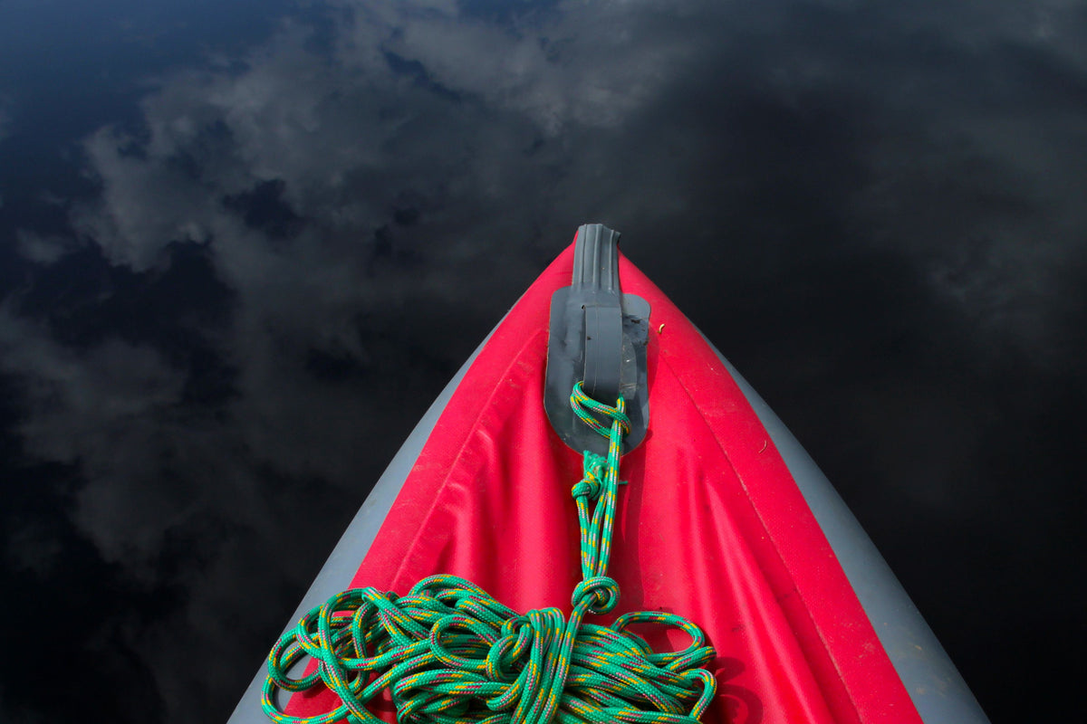 Top view of a kayak with colorful rope on calm water reflecting sky.