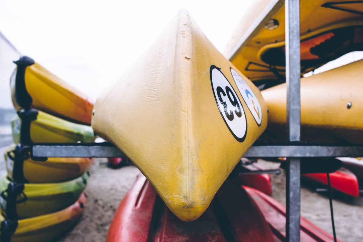 A detailed view of brightly colored kayaks stacked outdoors, focusing on a yellow kayak with numbers.