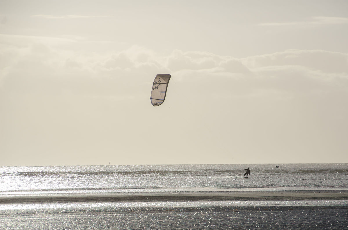 Silhouetted kite surfer enjoying sports on ocean waves during a serene sunset.