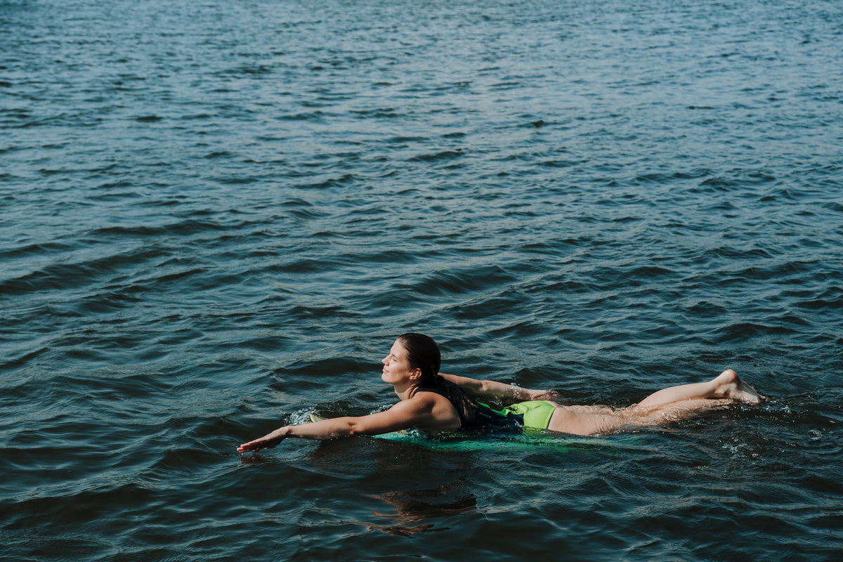 A woman enjoying a sunny day by paddling on a surfboard across the ocean waves.