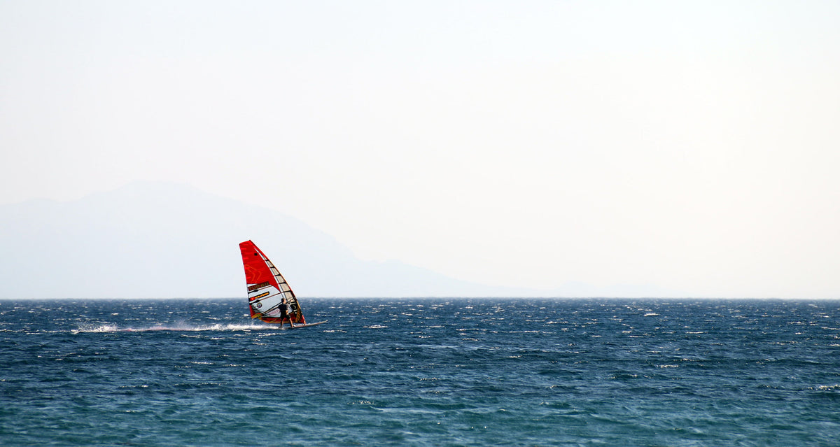 Experience the thrill of windsurfing across the vast sea under clear skies.